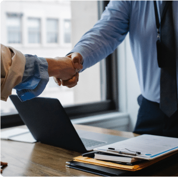 Two professionals shaking hands over a desk in an office.