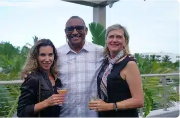 Three people smiling, holding drinks outdoors.