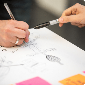 Two people collaborating on a sketch with pens and sticky notes.