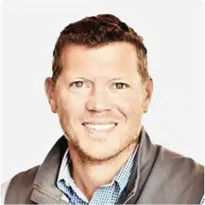 Smiling man with short hair wearing a gray jacket and blue checkered shirt.