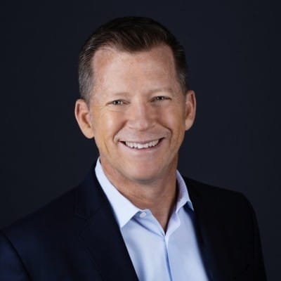Professional man in a dark suit smiling against a black background.
